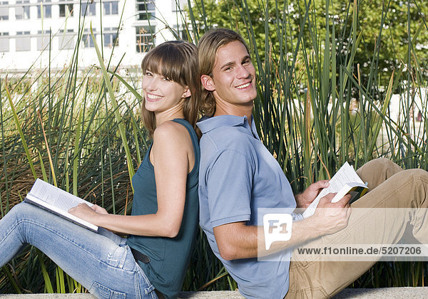 Studentenpaar  sitzen beim Lesen an Teich vor Uni  Rücken an Rücken