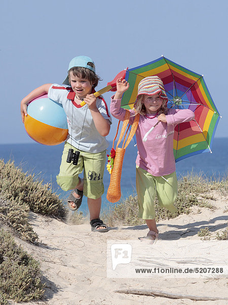 Zwei Kinder laufen am Meer über Dünen