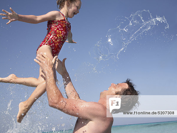 Vater mit kleiner Tochter am Strand  er wirft sie in die Luft