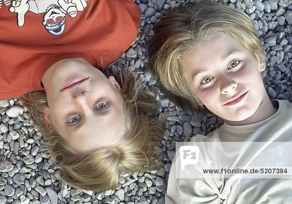 Zwei Jungen liegen nebeneinander auf Kiesboden  Halbporträt