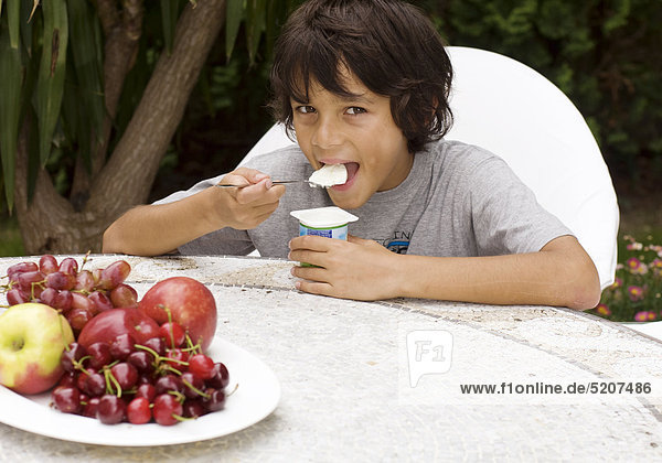 Junge sitzt an Gartentisch  isst Joghurt