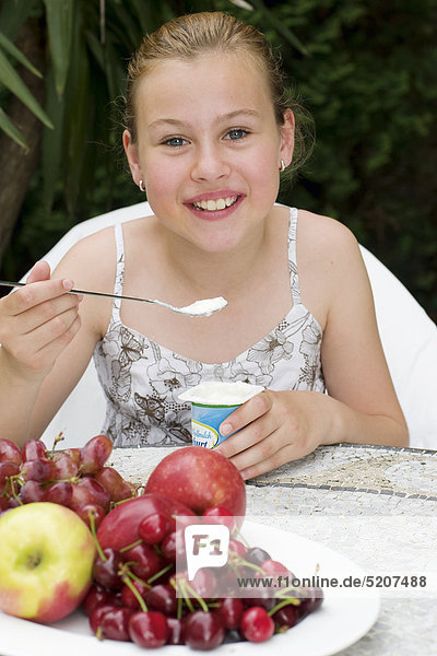Mädchen sitzt an Gartentisch  isst Joghurt