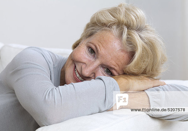 Seniorin auf Sofa  lächelnd Kopf auf Arme gelegt  Porträt
