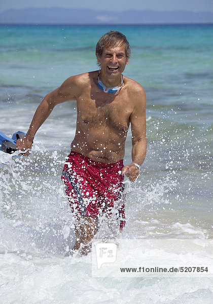 Älterer Mann läuft am Strand durch Wasser