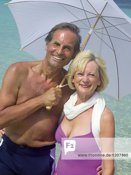 Älteres Paar mit Sonnenschirm am Strand  Halbporträt