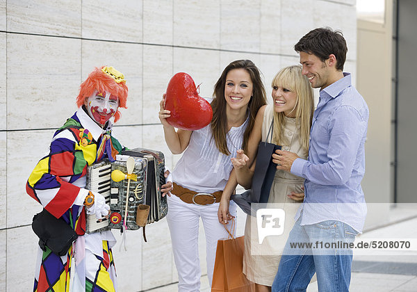 Zwei Frauen und ein Mann in der Stadt bei Clown mit Akkordeon