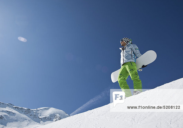 Mann steht mit Snowboard an Halfpipe