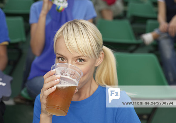 Weiblicher Fußballfan trinkt Bier aus Kunststoffbecher