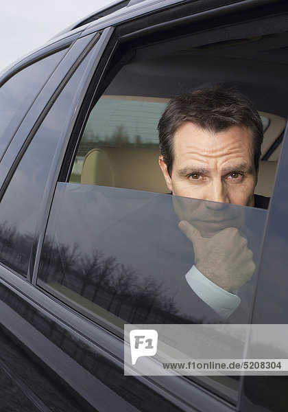 Mann schaut nachdenklich aus verdunkeltem Autofenster