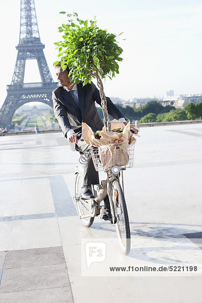 Businessman carrying a plant on a bicycle with the Eiffel Tower in the background  Paris  Ile-de-France  France