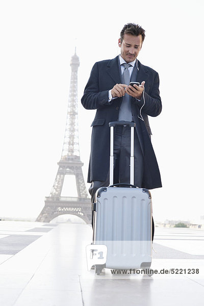Geschäftsmann stehend mit Gepäck auf dem Handy mit dem Eiffelturm im Hintergrund  Paris  Ile-de-France  Frankreich
