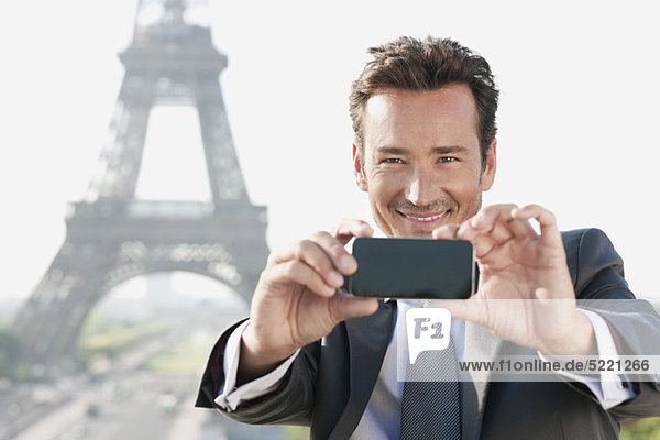 Geschäftsmann beim Fotografieren mit dem Handy mit dem Eiffelturm im Hintergrund  Paris  Ile-de-France  Frankreich