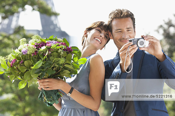 Woman holding a bouquet of flowers and man showing pictures in a digital camera with the Eiffel Tower in the background  Paris  Ile-de-France  France