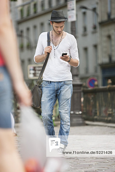 Man walking on the road and text messaging with a mobile phone,  Paris,  Ile-de-France,  France
