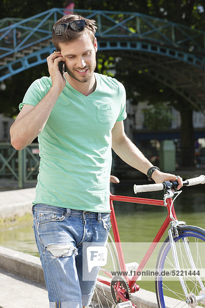 Mann  der mit dem Fahrrad geht und mit dem Handy spricht  Paris  Ile-de-France  Frankreich