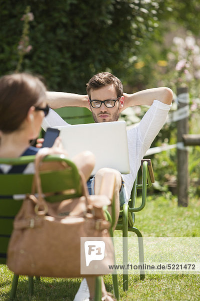 Mann sitzt in einem Garten und schaut auf einen Laptop  Paris  Ile-de-France  Frankreich