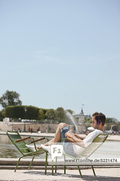 Mann  der auf einem Stuhl sitzt und eine Zeitschrift liest  Bassin achteckig  Jardin des Tuileries  Paris  Ile-de-France  Frankreich