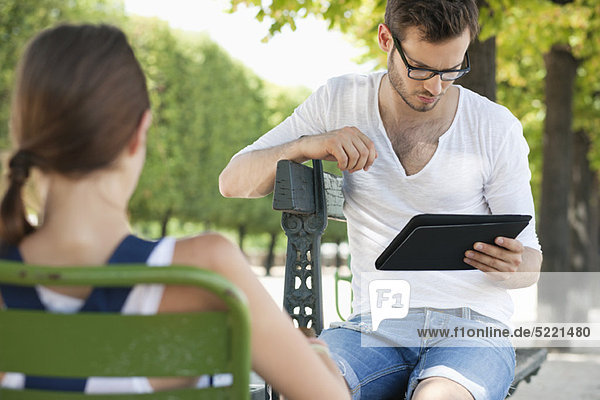 Man using a digital tablet with a woman sitting in front of him  Jardin des Tuileries  Paris  Ile-de-France  France
