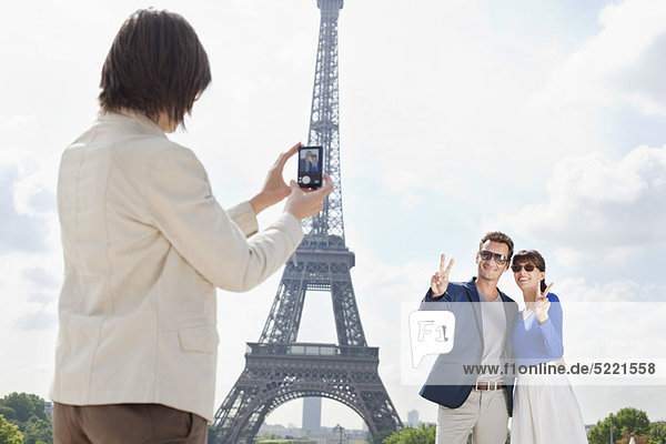 Woman taking a picture of couple with the Eiffel Tower in the background  Paris  Ile-de-France  France