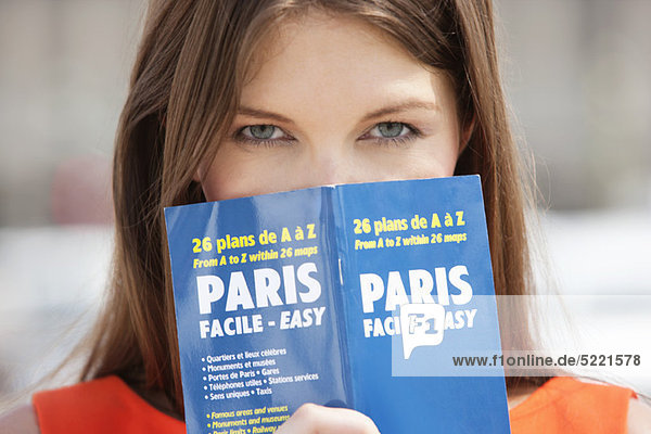 Porträt einer Frau mit einem Reiseführer vor dem Gesicht  Paris  Ile-de-France  Frankreich