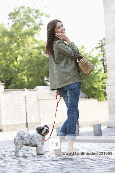 Woman holding a puppy on leash while talking on a mobile phone  Paris  Ile-de-France  France