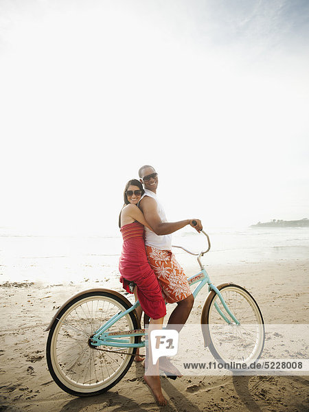 Couple riding retro bicycle on beach