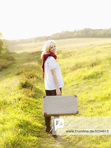 A woman walking in the country carrying a suitcase