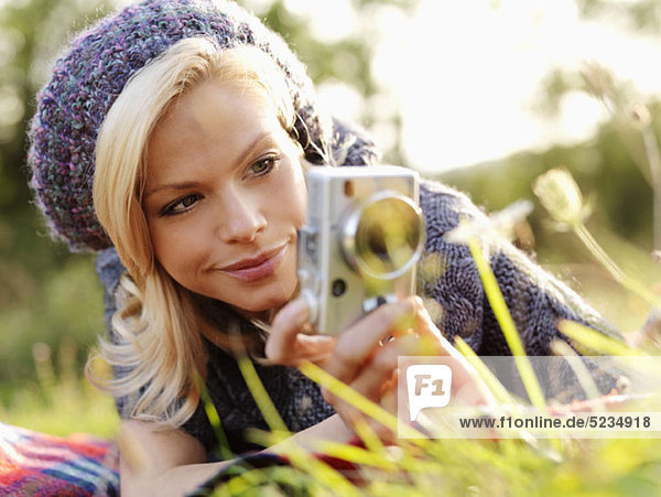 A woman photographing while lying in grass