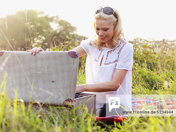 A woman sitting in the grass rummaging through an open suitcase