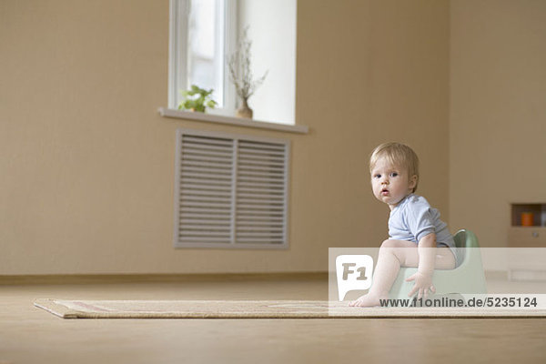 Ein Kleinkind sitzt auf einem Töpfchenstuhl und schaut in die Kamera.