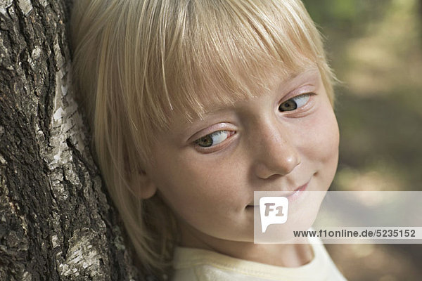 A young girl leaning against a tree  sideways glance