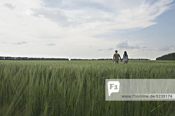 Ein Mann und eine Frau gehen Hand in Hand durch ein abgelegenes Weizenfeld.