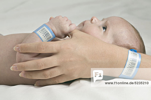 Ein Baby  das den Daumen seiner Mutter hält  beide mit Krankenhausarmbändern.