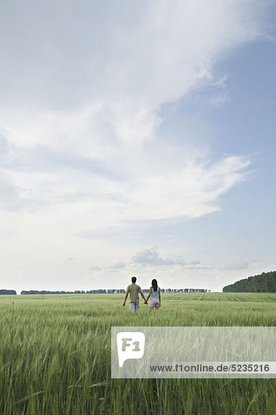 Ein Mann und eine Frau gehen Hand in Hand durch ein abgelegenes Feld.