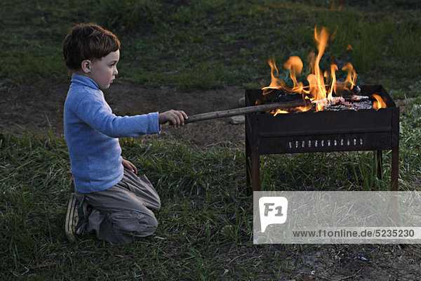 Ein Junge  der ein Feuer in einer Feuerstelle im Freien anstößt.