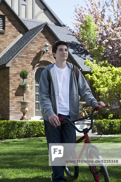 Junge geht auf Rasen und hält sein Fahrrad an seiner Seite.