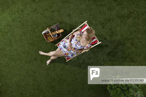 Eine Frau sitzt in der Sonne auf einem Gras in einem Park mit Picknickkorb  Blick nach oben
