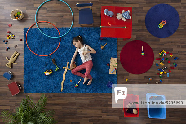 Ein kleines Mädchen liegt auf einem Teppich mit Spielzeug  Blick nach oben