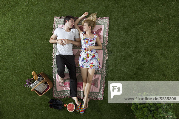 Ein Paar  das auf einer Decke in einem Park liegt und sich romantisch ansieht.