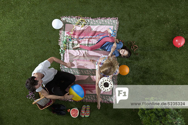 Eine Familie feiert bei einem Picknick im Park mit Kuchen  Luftballons und Luftschlangen  Blick nach oben.
