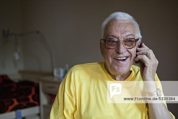 Ein fröhlicher älterer Mann  der in einem Pflegeheim lebt und ein Handy benutzt.