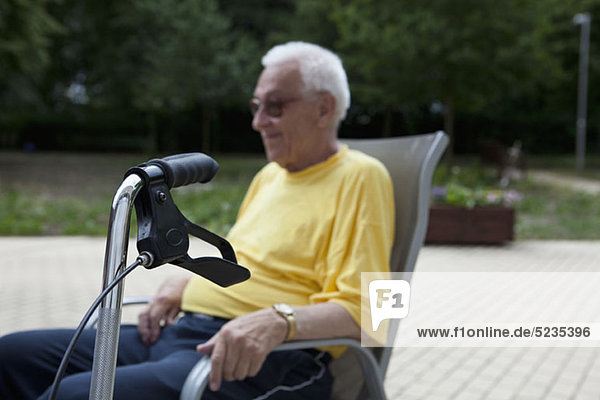 A senior man sitting in a chair  the handle of his walker in the foreground  focus on foreground