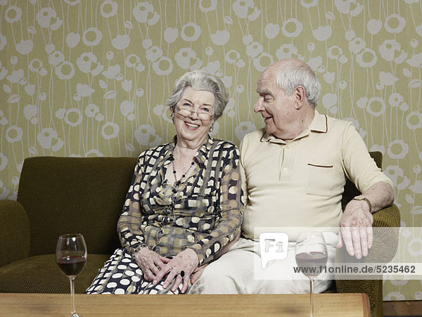 Seniorenpaar entspannt auf der Couch mit zwei Gläsern Wein auf dem Tisch