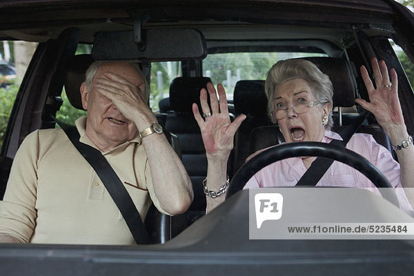 Senior woman having trouble learning to drive as man in passenger seat despairs