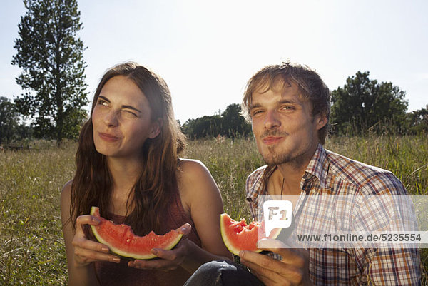 Couple sitting eating melon in field