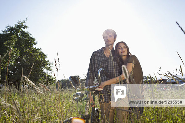 Couple with arms around each other walk through field with bike