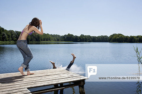 Der Typ spritzt vom Steg ins Wasser  während das Mädchen zusieht.