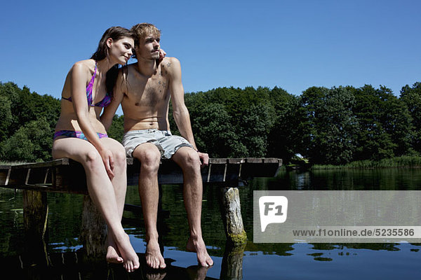 Couple sitting on edge of jetty by lake