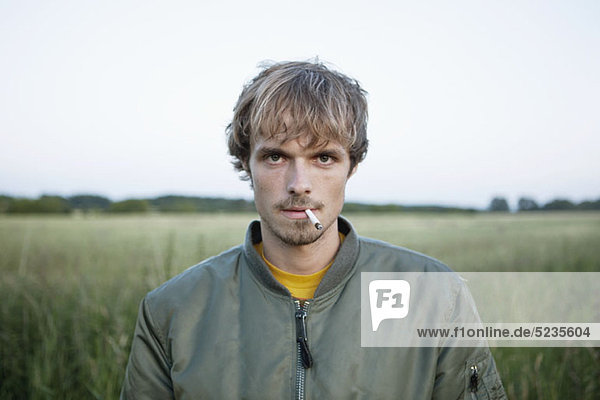 Profil eines Mannes  der auf einem abgelegenen Feld steht und eine Zigarette aus dem Mund hängt.