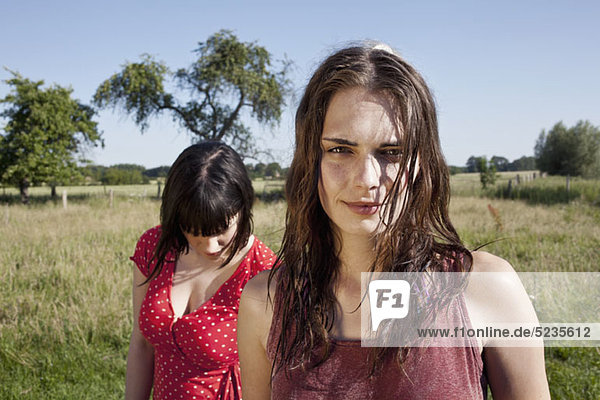 Two cool girls standing in field with one looking at camera